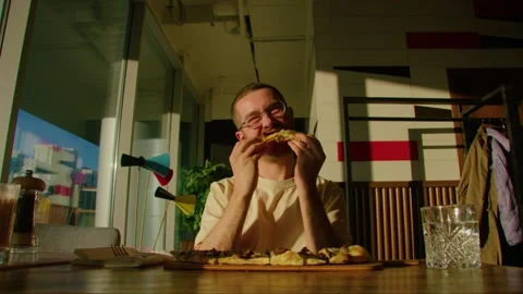 Bearded man looking at the camera, eating pizza and smiling in a restaurant Stockbeeldmateriaal 244085017