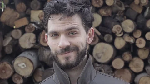 Bearded Man Looking Confident into the Camera with Wooden Logs in Background Stock Footage 239654541