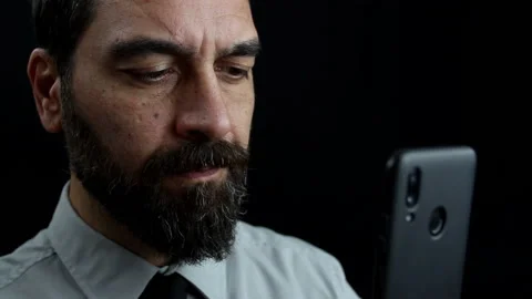 Bearded man looks and types on mobile while holding it in hand Stock Footage 143486216