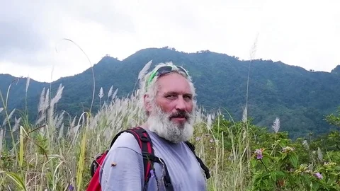 A bearded man looks at the camera and goes into the mountains. Video stock 122369605
