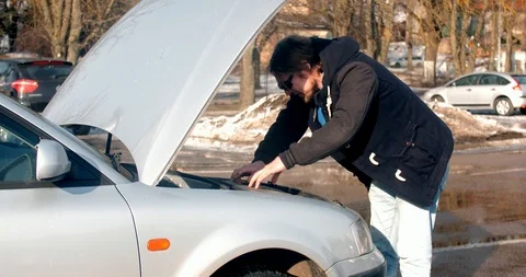 Bearded man looks for errors in the car at market parking Stock Footage 86978489