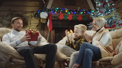Bearded man looks inside his Christmas present sitting with wife and son while Stock Footage 100229960