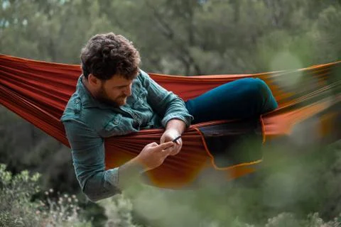 Bearded man lying in a hammock using his mobile phone Stock Photos