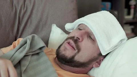 A bearded man measures his temperature with a medical thermometer. He has a cold Stockbeeldmateriaal 96321549