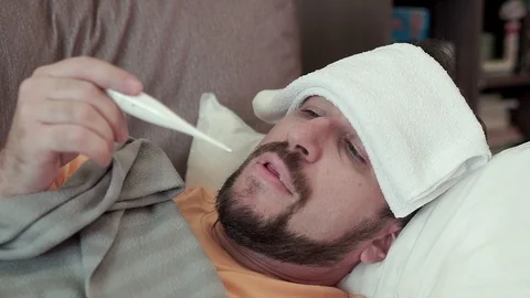 Bearded man measures his temperature, looks at the thermometer. He has a cold Stock Footage 96321614