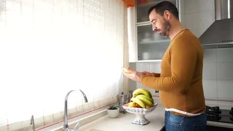 Bearded man in an orange sweater picking up a banana and making a thumbs up g Stock Footage 149397599