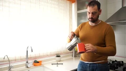 Bearded man in an orange sweater pouring himself a cup of hot coffee Stock Footage 149397600