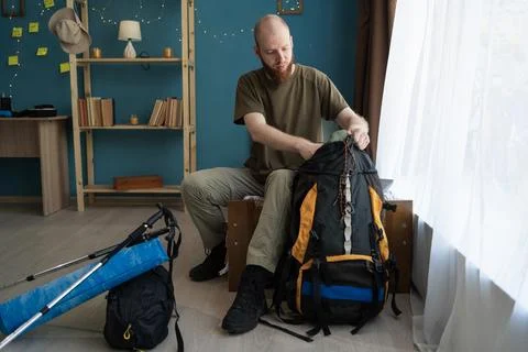 Bearded man packing backpack preparing for hiking trip putting away equipment Stock Photos