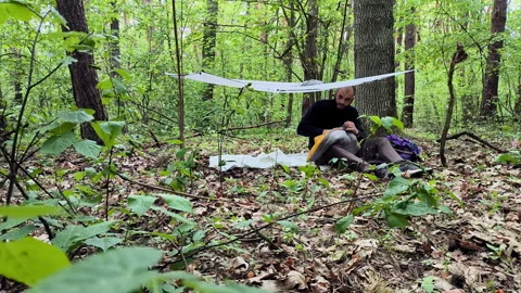 Bearded man packing down quilt into compression sack at campsite Video stock 336970019