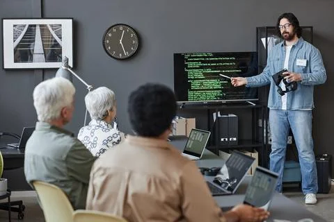 Bearded man pointing at screen with code teaching senior people in IT 스톡 사진