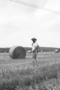 Bearded man posing while walking through field with many bales of straw. Stock Photos