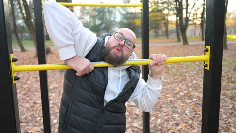 Bearded man practicing pull-ups in park surrounded by autumn leaves during Stock Footage 346541970