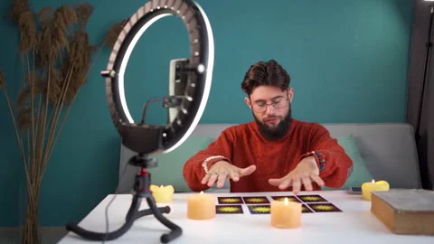 Bearded man predicting the future using tarot cards broadcasts live in his home Stock Footage 253789078