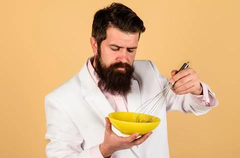 Bearded man preparing eggs for breakfast. Whisking egg in bowl for cooking om Stock Photos