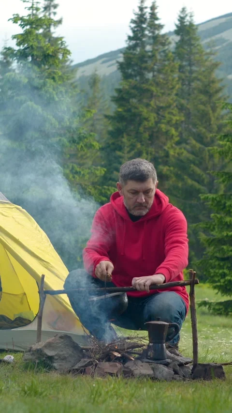 Bearded man preparing food on the fire in the mountains 库存影片 334389927