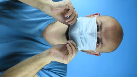 Bearded man puts on a face mask on a blue background, vertical video Stock Footage 141639927