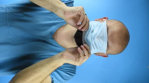 Bearded man puts on a face mask on a blue background, vertical video Vidéo 141790370