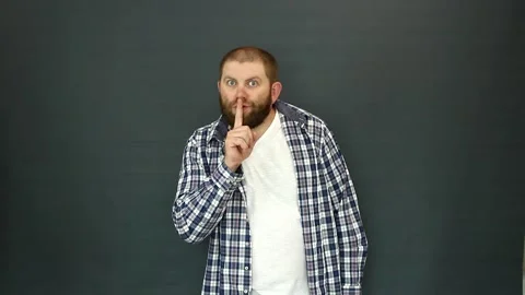 A bearded man puts his index finger to his lips on a gray background. Video stock 157859629