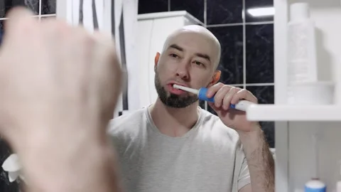 Bearded man puts toothpaste on electric brush and brushes his teeth Stock Footage 229531483