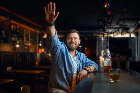 Bearded man with raised hand sitting in bar Stock Photos
