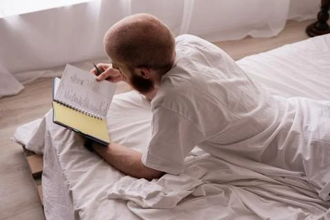 Bearded man reading notes in his private diary while lying on the bed in th.. Stock Photos