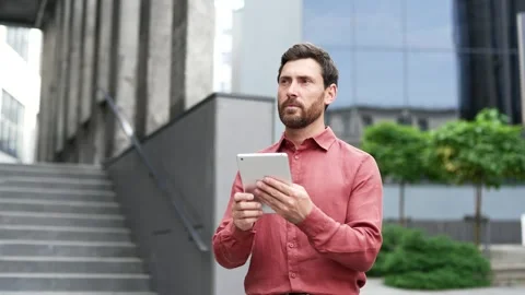 Bearded man in red shirt standing outside office building using digital tablet.  Stock Footage 283676829