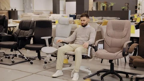 Bearded man relaxing in ergonomic office chair, finding comfort in showroom Stock Footage 334654121