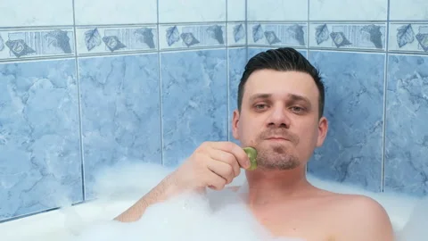 Bearded man relaxing lying in bath doing face massage using gouache scraper. Video stock 158922143