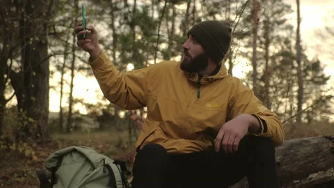 A bearded man rests on a fallen tree in the middle of the forest. A man uses a m Video stock 220189214