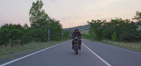 Bearded man rides old cafe racer motorcycle on country road, evening Stock Footage 140623079