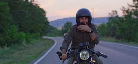 Bearded man rides old cafe racer motorcycle on country road, evening, bad smell Stock Footage 140623080