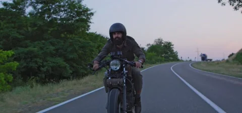 Bearded man rides old cafe racer motorcycle on country road, evening Stock Footage 140623097