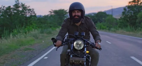 Bearded man rides old cafe racer motorcycle on country road, evening Stock Footage 140623101
