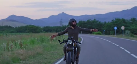Bearded man rides old cafe racer motorcycle on country road, evening Stock Footage 140623168