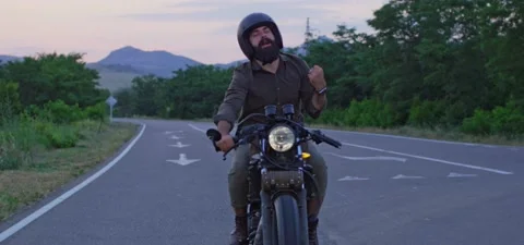 Bearded man rides old cafe racer motorcycle on country road, evening Stock Footage 140623272