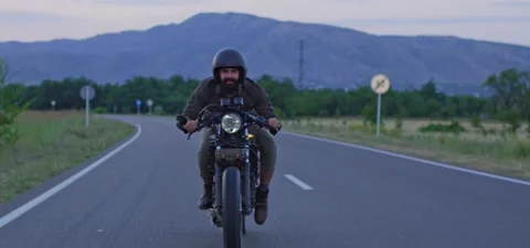 Bearded man rides old cafe racer motorcycle on country road, evening Stock Footage 140623295
