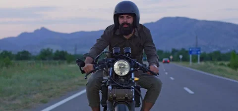 Bearded man rides old cafe racer motorcycle on country road Stock Footage 140623325