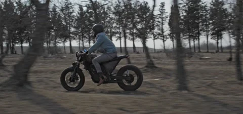 Bearded man rides old cafe racer motorcycle between trees Stock Footage 140626329