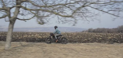Bearded man rides old cafe racer motorcycle between trees on field Stock Footage 140626333