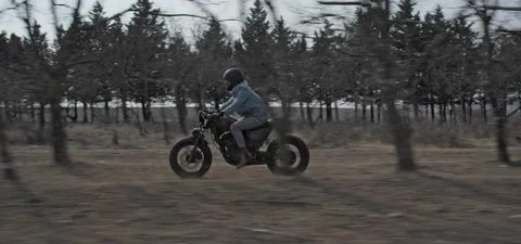 Bearded man rides old cafe racer motorcycle between trees Stock Footage 140626440