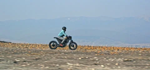 Bearded man rides old cafe racer motorcycle on open field near mountains Stock Footage 140626622