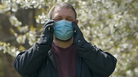 A bearded man in rubber gloves puts on a medical mask against the background Stock Footage 129283749
