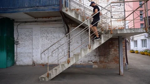 Bearded man runs down a staircase with rusty railing in sunny day. Old district. Stock Footage 125456341