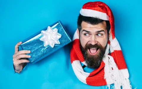 Bearded man in santa hat with present gift box looking through paper hole. .. Stock Photos