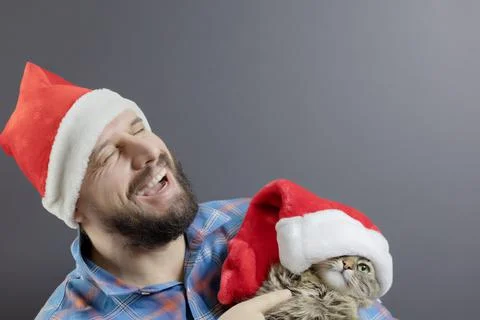 A bearded man in Santa's hat laughs from the cat in the red hat pointing at him Stock Photos