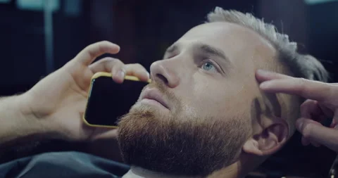 Bearded man, shortens his beard in the beauty salon and talks on the phone Stock Footage 139965874