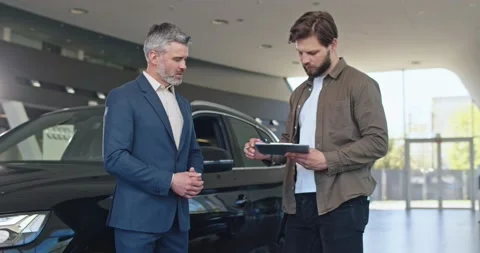 Bearded man is signing documents at car center. He is shaking hands with car Stock Footage 156543678