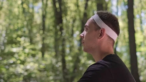 A bearded man sits in the forest on a mat, practicing meditation while listening Stock Footage 280186353
