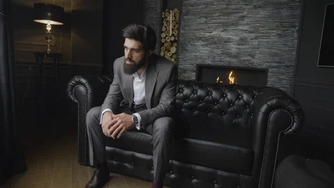 Bearded man sits on sofa at decorated wall with fireplace Stock Footage 103924768