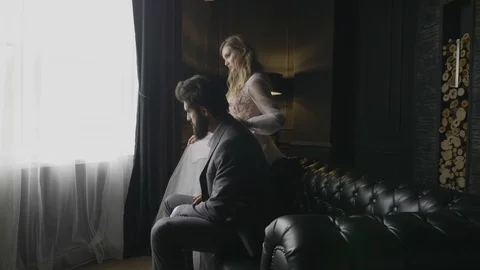 Bearded man sits on sofa lady touches shoulder at window Stock Footage 103924779